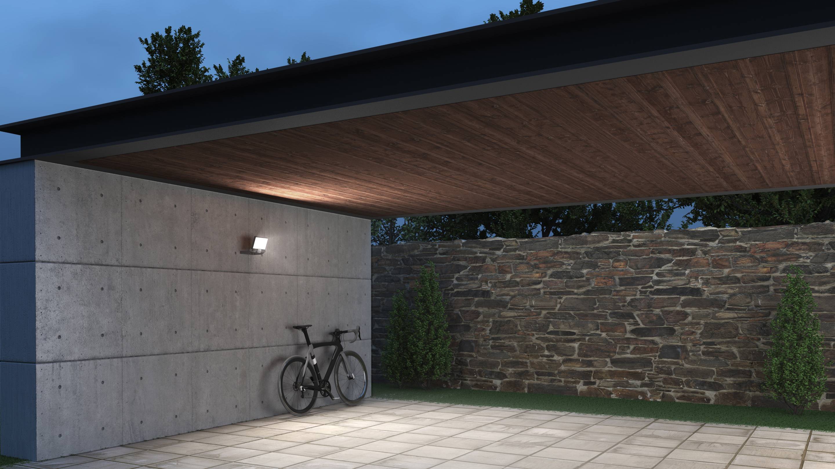 Garage moderne avec plafond en bois et éclairage, vélo appuyé contre un mur en béton, mur de pierre en arrière-plan, entouré d'arbres.