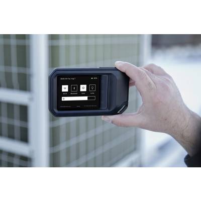 Une personne tient un appareil électronique portable avec un écran qui affiche une interface utilisateur avec des icônes. En arrière-plan, un environnement extérieur flou.