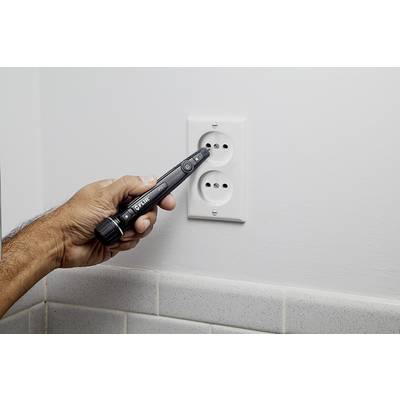 Une main tient un testeur de tension près d'une prise électrique pour vérifier le courant.