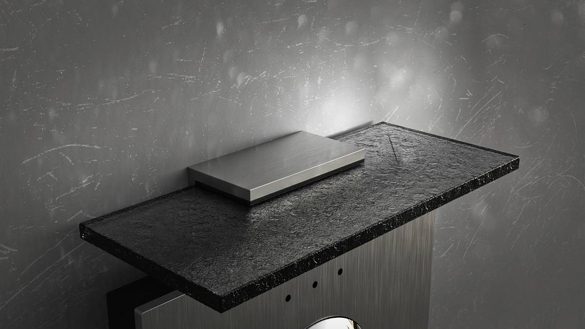 Une console murale élégante, minimaliste, sombre et rectangulaire en pierre noire, sur laquelle repose un objet métallique argenté, devant un mur texturé.