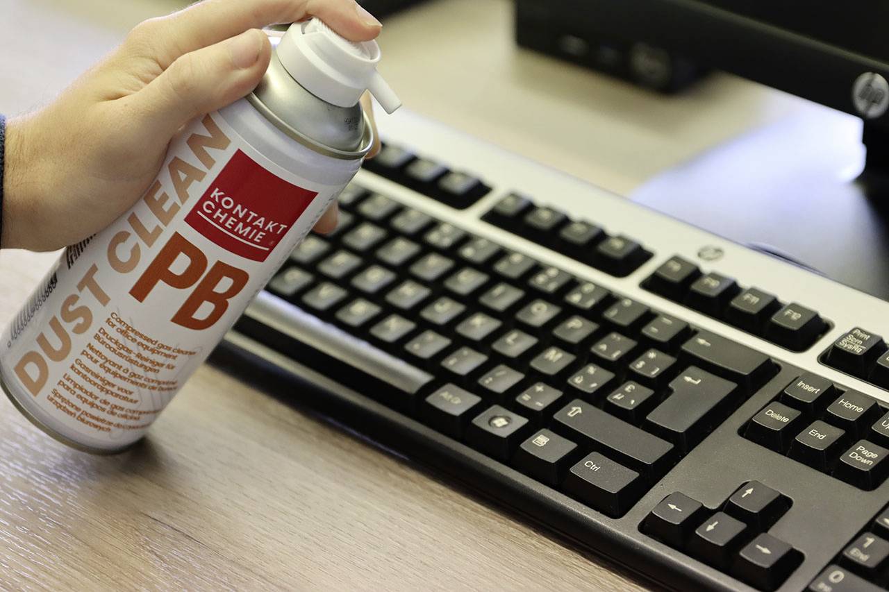 Une main tient une bombe d'air comprimé au-dessus d'un clavier d'ordinateur pour enlever la poussière.