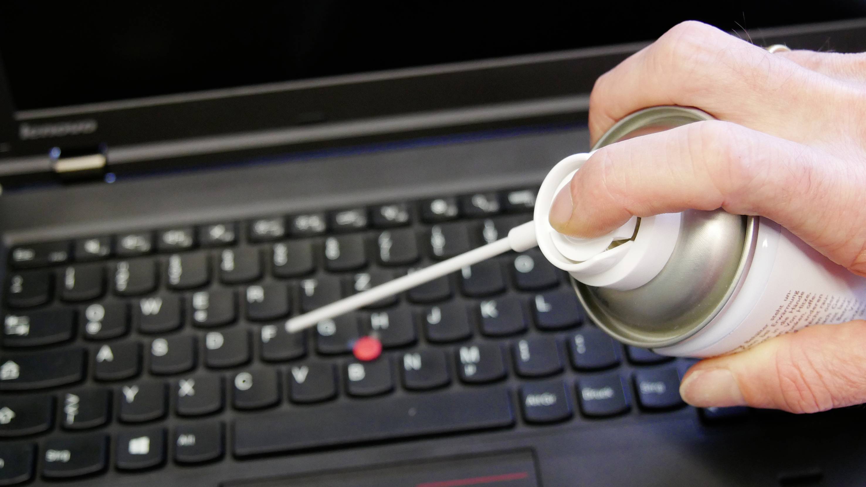 Une main pulvérise de l'air comprimé sur le clavier d'un ordinateur portable pour le nettoyer.