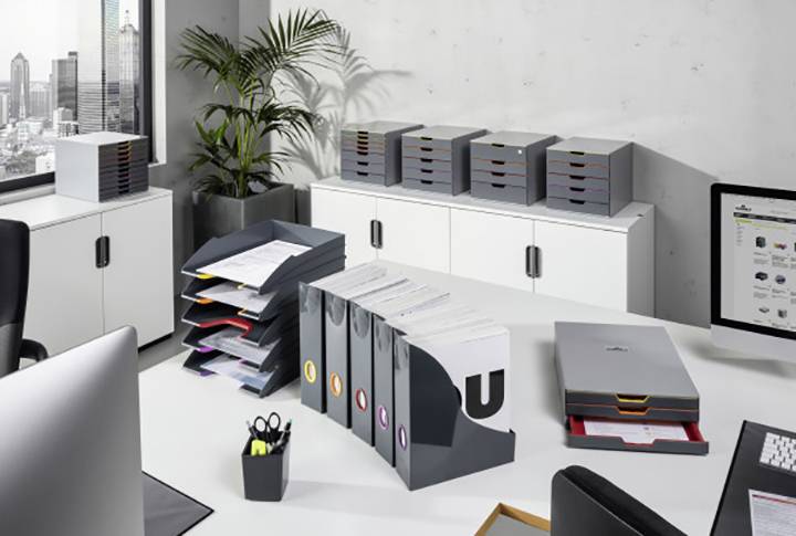 Un bureau moderne avec des meubles blancs, plusieurs classeurs et supports de documents sur le bureau. Vue sur la ville en arrière-plan depuis la fenêtre.