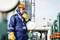 Un travailleur en tenue de sécurité et casque vérifie une installation dans un site industriel à l'aide d'une radio. Il porte des protections auditives.