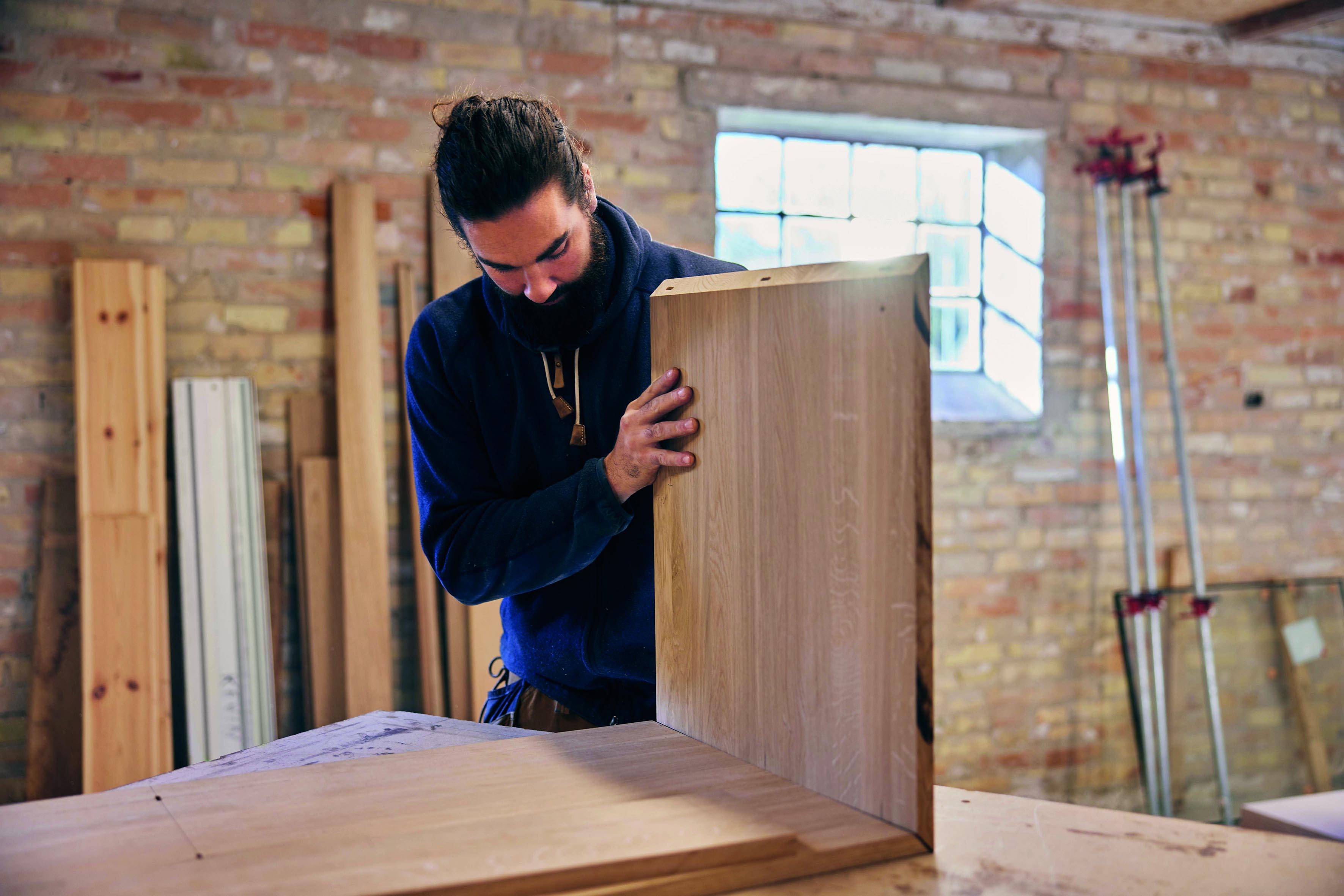 Un menuisier se penchant sur un grand panneau d'armoire dans un atelier, assemblant ou inspectant des pièces de mobilier.