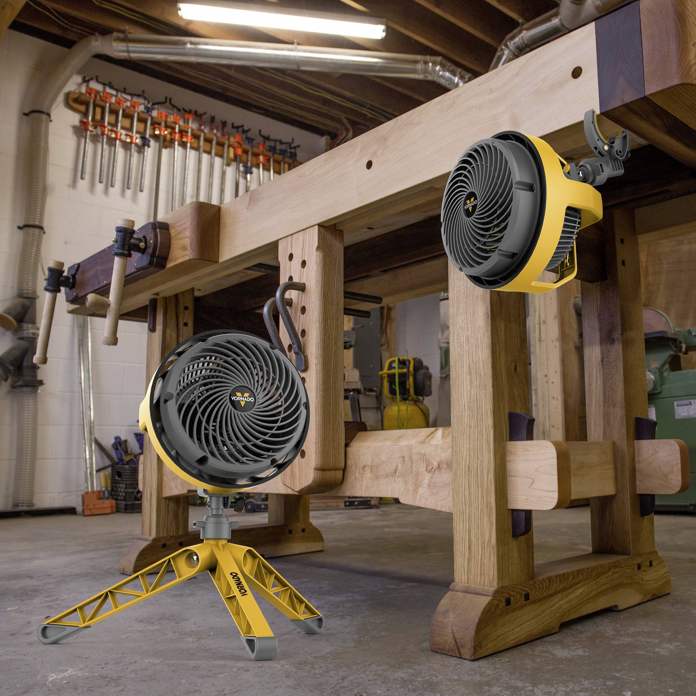 Deux ventilateurs jaunes placés sur une table en bois dans un atelier. Des outils sont visibles en arrière-plan.