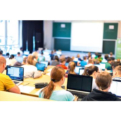 Des étudiants dans un amphithéâtre travaillent sur des ordinateurs portables ; le cours est projeté sur un écran.
