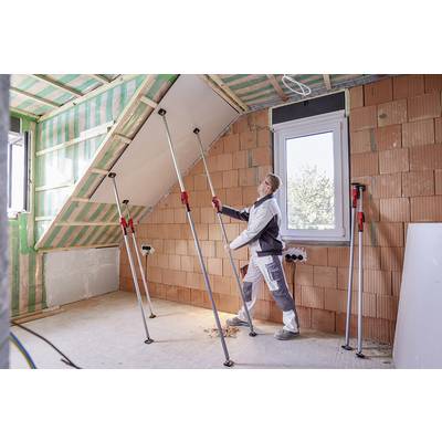 Une personne travaille à la rénovation d'un grenier, soulève une plaque de plâtre au plafond à l'aide de supports télescopiques pour la soutenir.