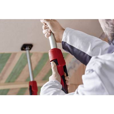 Une personne installe une barre métallique avec une poignée rouge entre le sol et le plafond, probablement pour faciliter des travaux de construction.