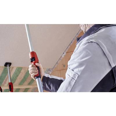 Une personne ajuste une perche télescopique rouge dans un chantier de construction pour la réalisation de plafonds.