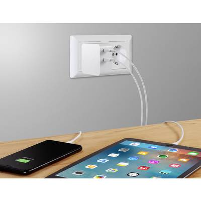 Un smartphone et une tablette sont en cours de chargement sur une table, tous deux connectés à un adaptateur double sur une prise murale.