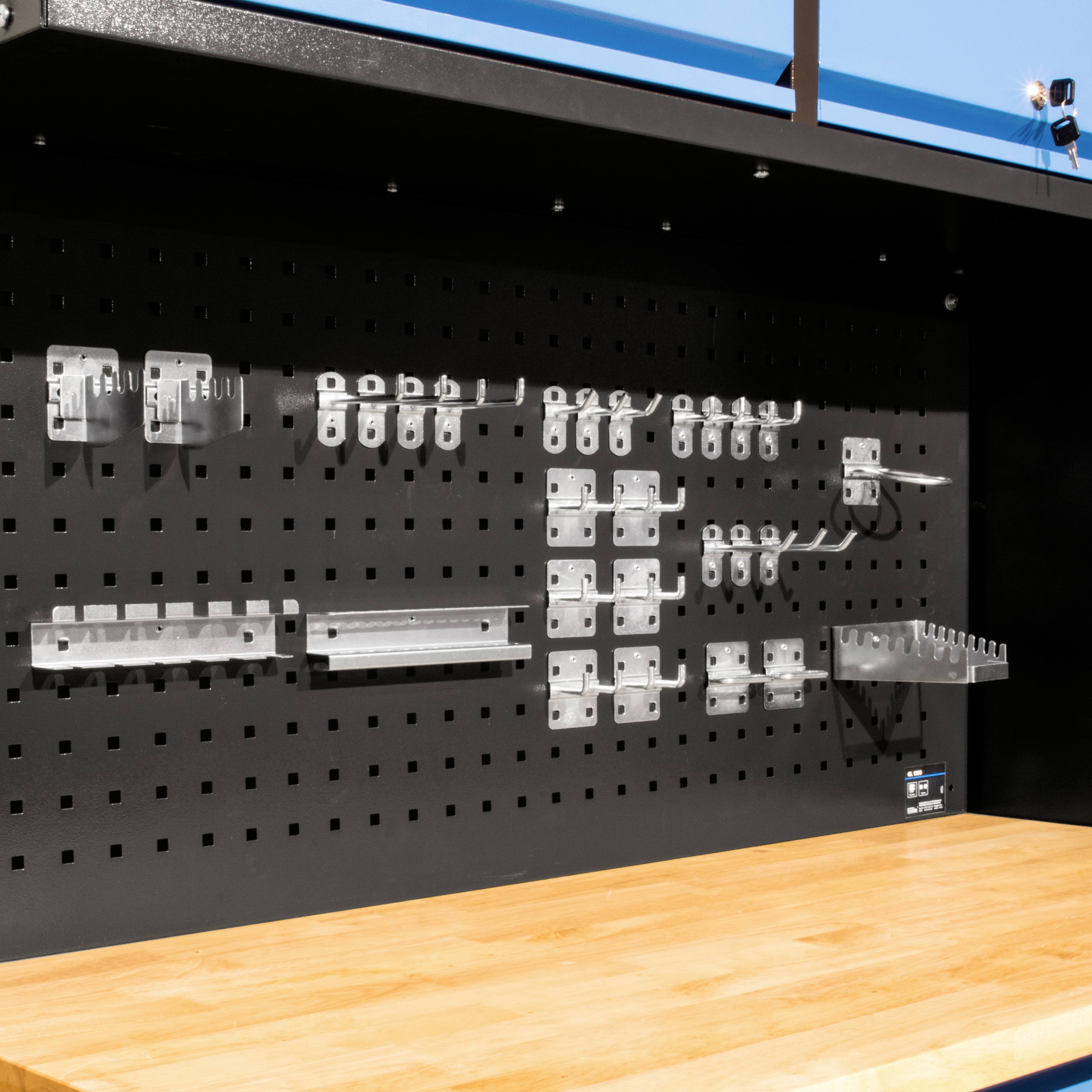 Étagère murale à outils noire avec crochets et supports métalliques, montée sur un établi en bois. Un panneau bleu en arrière-plan.