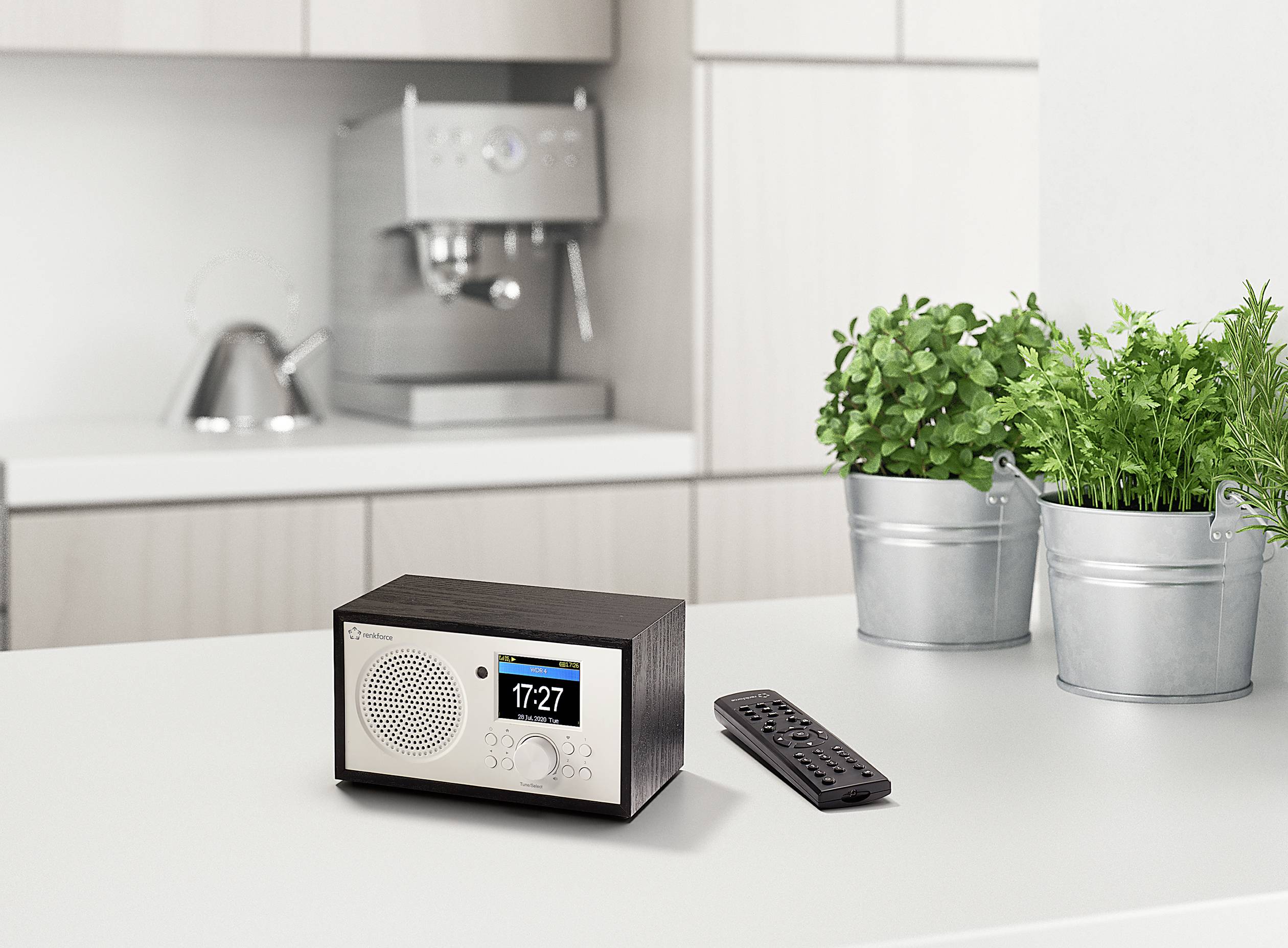 Une radio sur un plan de travail de cuisine, à côté d'un appareil de télécommande. Une machine à café est visible en arrière-plan.