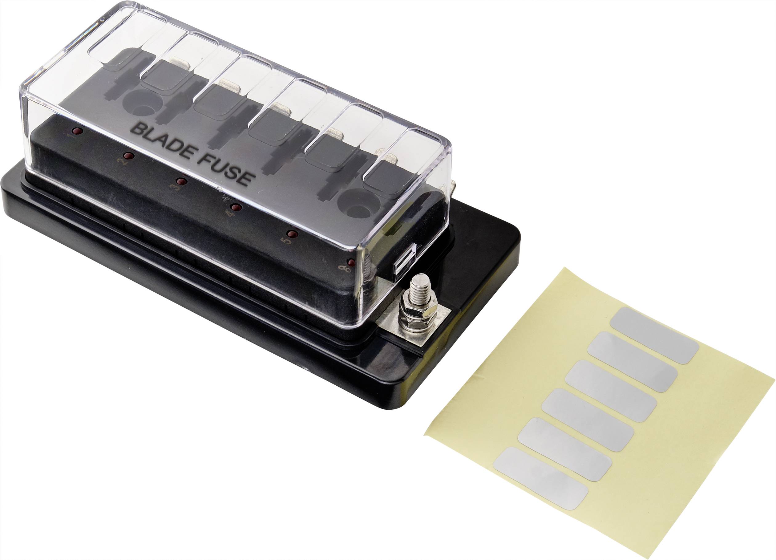 Boîte de fusibles avec couvercle transparent, contenant plusieurs fusibles plats. À côté, une feuille avec des autocollants argentés.