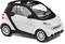 Une petite voiture à deux places avec un toit noir et un corps blanc, adaptée aux trajets urbains, sur un fond blanc.