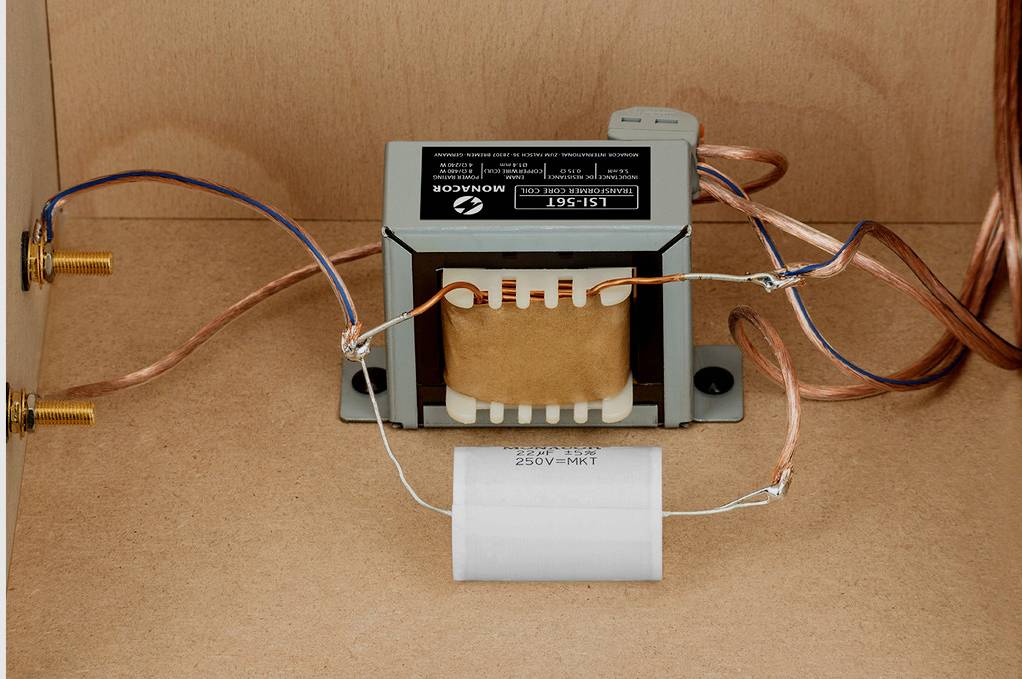 Un filtre de fréquence pour haut-parleur avec bobine, condensateur et fils, monté dans un boîtier en bois.