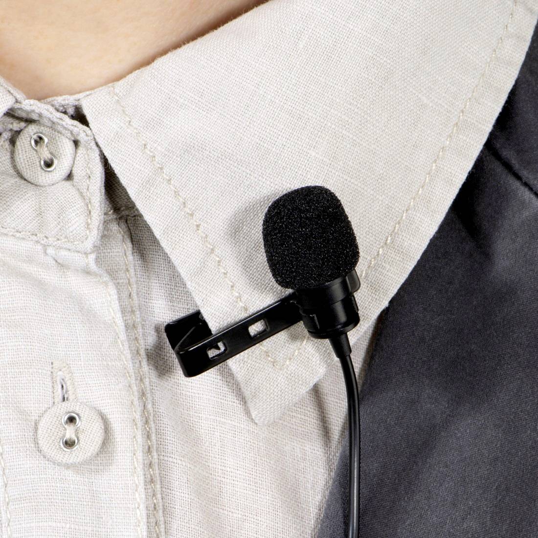 Une personne porte un microphone fixé à son col de chemise. Le microphone est noir et petit, idéal pour les enregistrements.