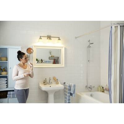 Une femme se tient dans une salle de bain et se brosse les dents devant un miroir. À l'arrière-plan, on peut voir un lavabo, une baignoire et un rideau de douche.