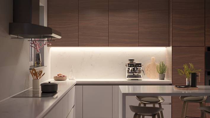 Cuisine moderne avec des armoires en bois, une machine à café sur le plan de travail et un éclairage lumineux. Un meuble à tiroirs et des articles de décoration sont visibles.