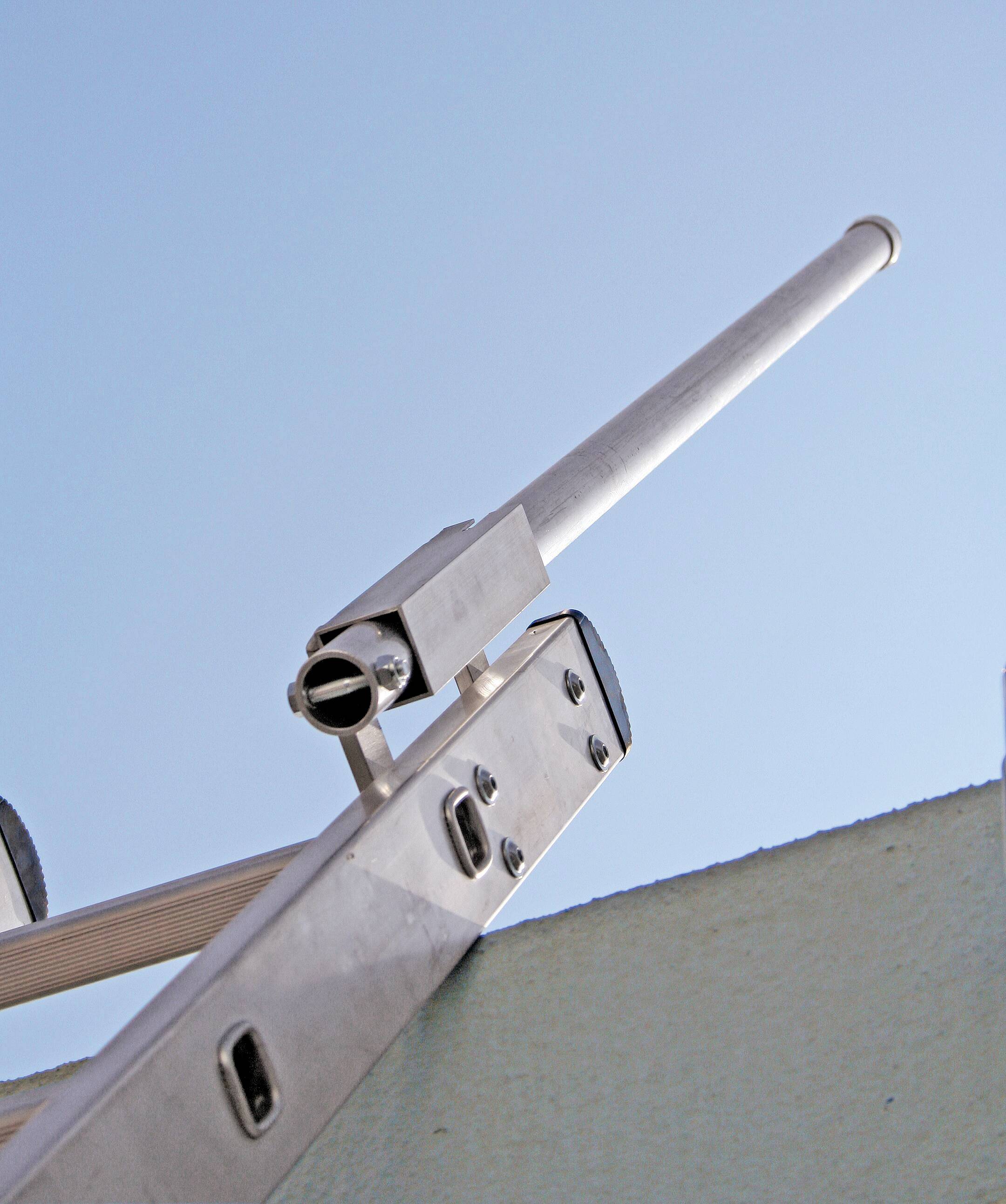 Une longue antenne métallique est fixée à un mât et s'élève dans le ciel bleu, probablement destinée à la transmission de signaux.