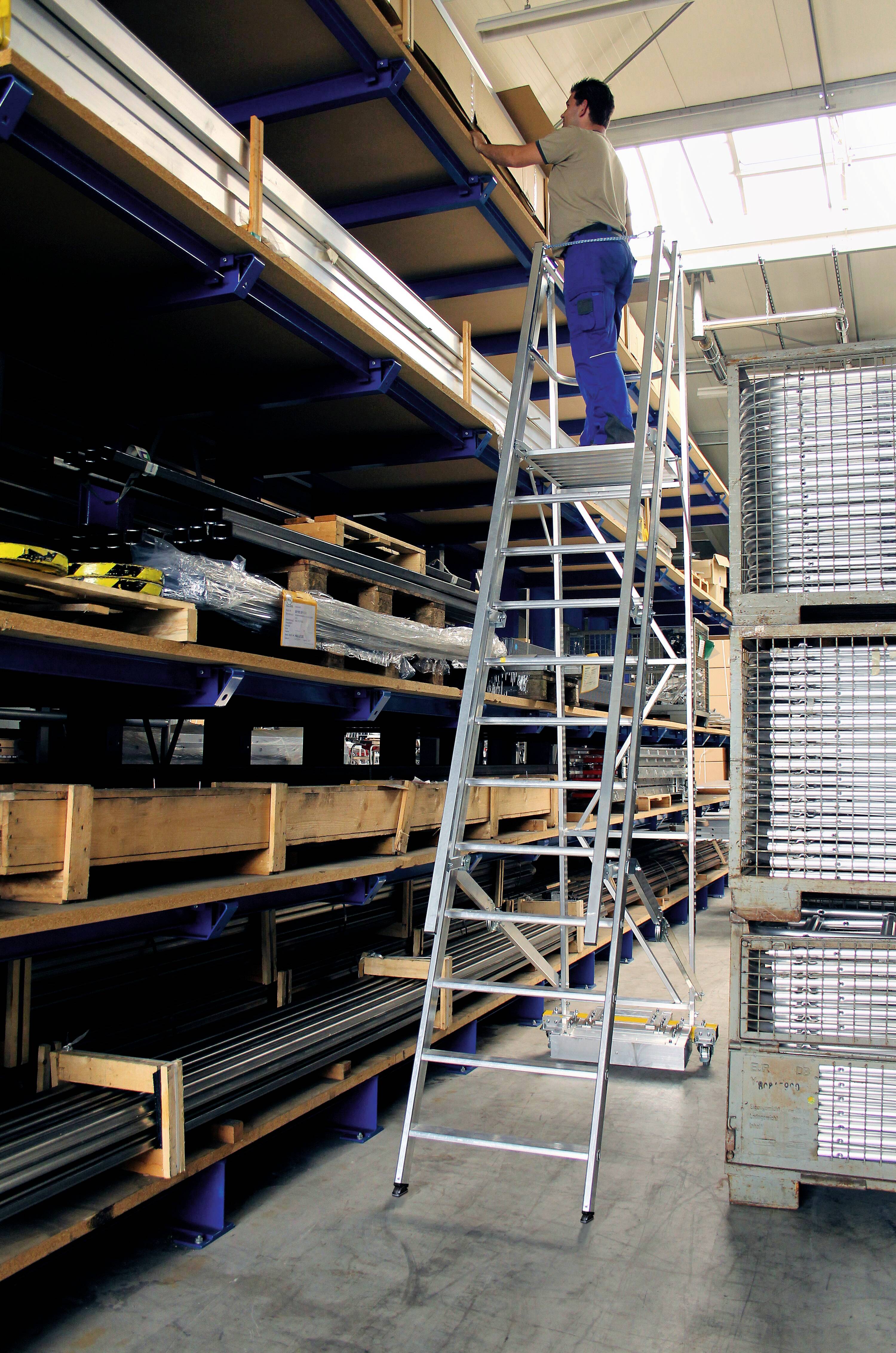 Un homme se tient sur une échelle haute et tend la main vers un objet sur une étagère supérieure dans un entrepôt avec des étagères métalliques et des caisses.