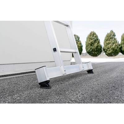 Un escabeau stable en aluminium est solidement placé sur une surface d'asphalte, avec des arbres flous en arrière-plan.