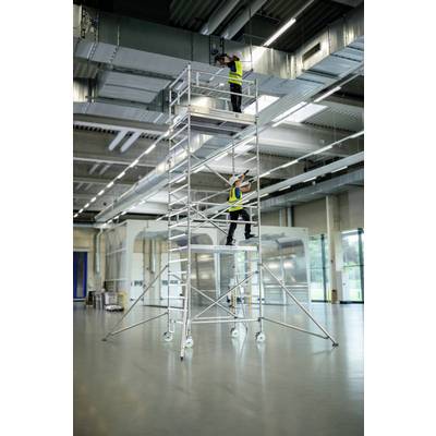 Deux personnes travaillent sur un échafaudage dans une grande halle. Elles portent des gilets de sécurité et des casques.