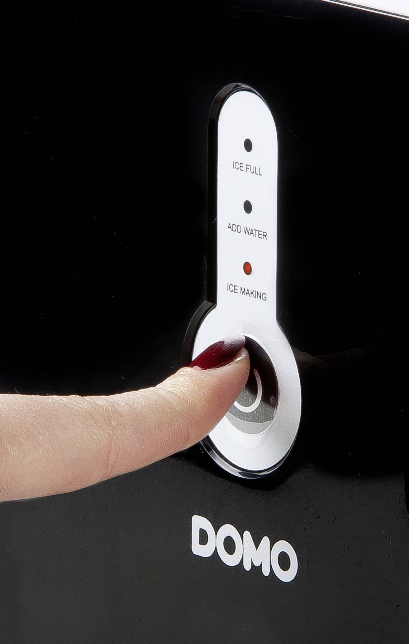 Une main portant du vernis à ongles rouge appuie sur le bouton d'un appareil portant l'inscription 'DOMO'. Les indicateurs affichent 'Glace Pleine', 'Ajouter Eau', 'Fabrication de Glace'.
