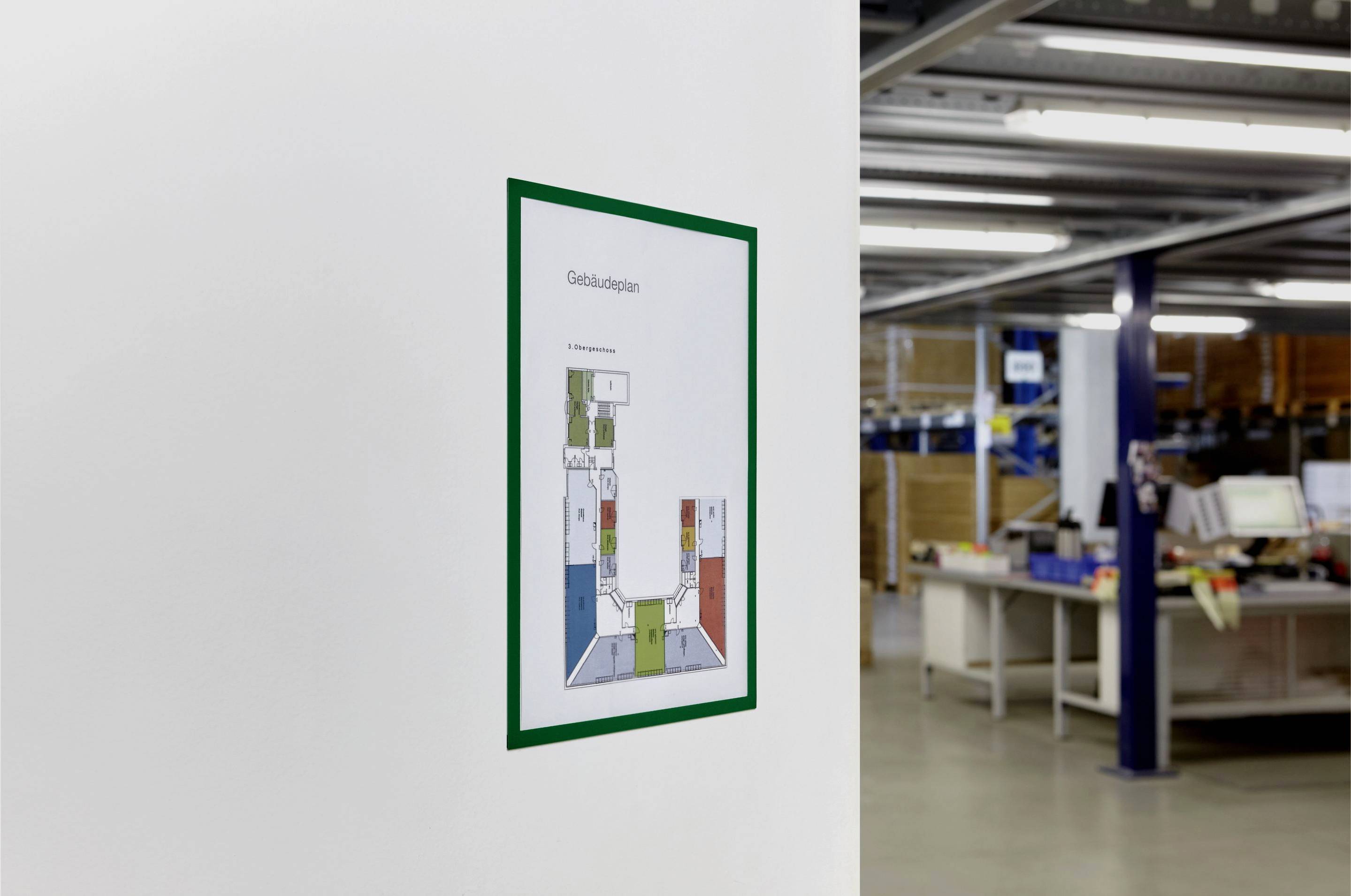 Un plan de bâtiment est accroché au mur dans un espace de bureau. Des étagères et des bureaux sont visibles en arrière-plan.