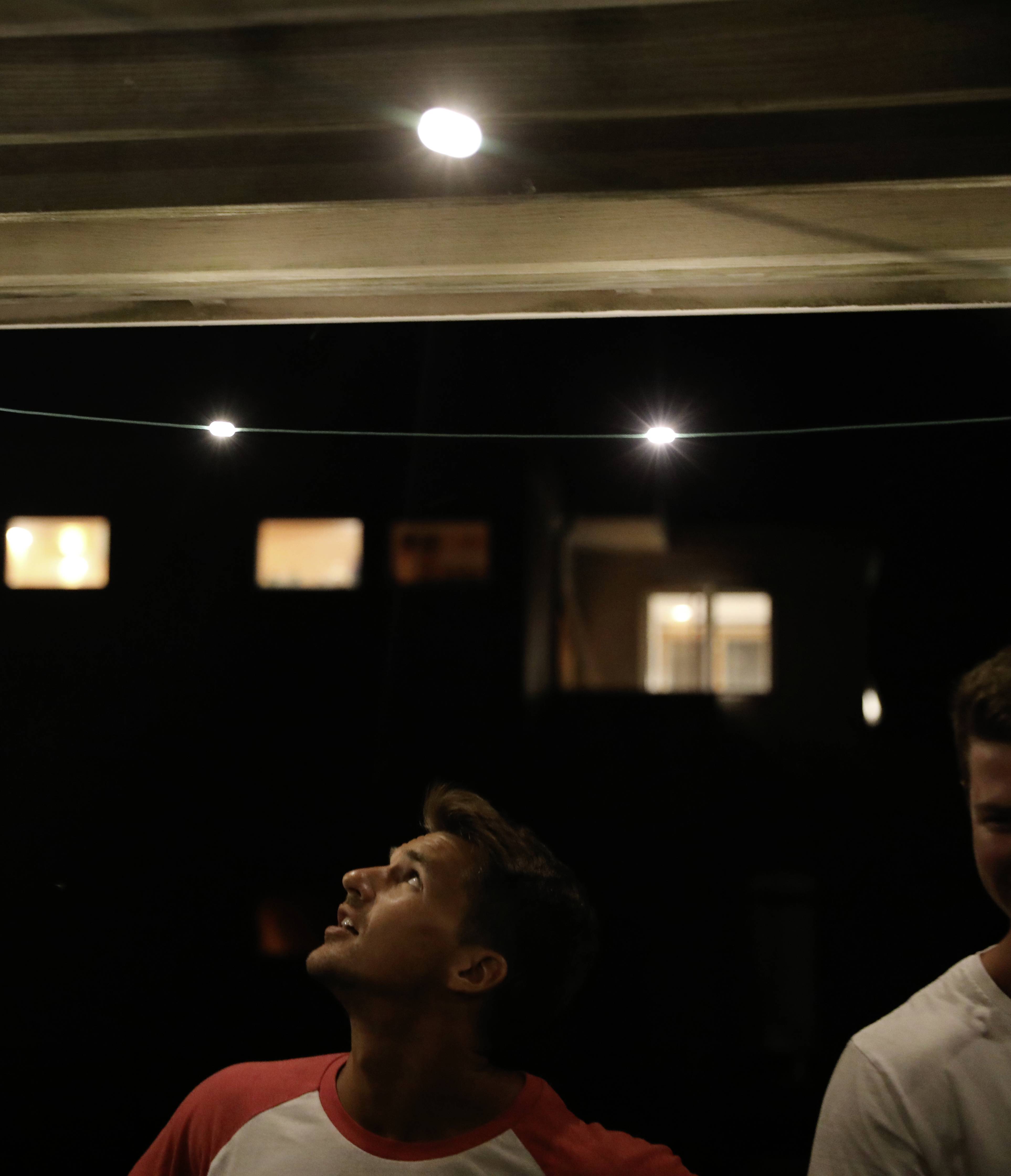 Une personne regarde vers le haut des lumières sur une terrasse la nuit. Des fenêtres éclairées de bâtiments sont visibles en arrière-plan.