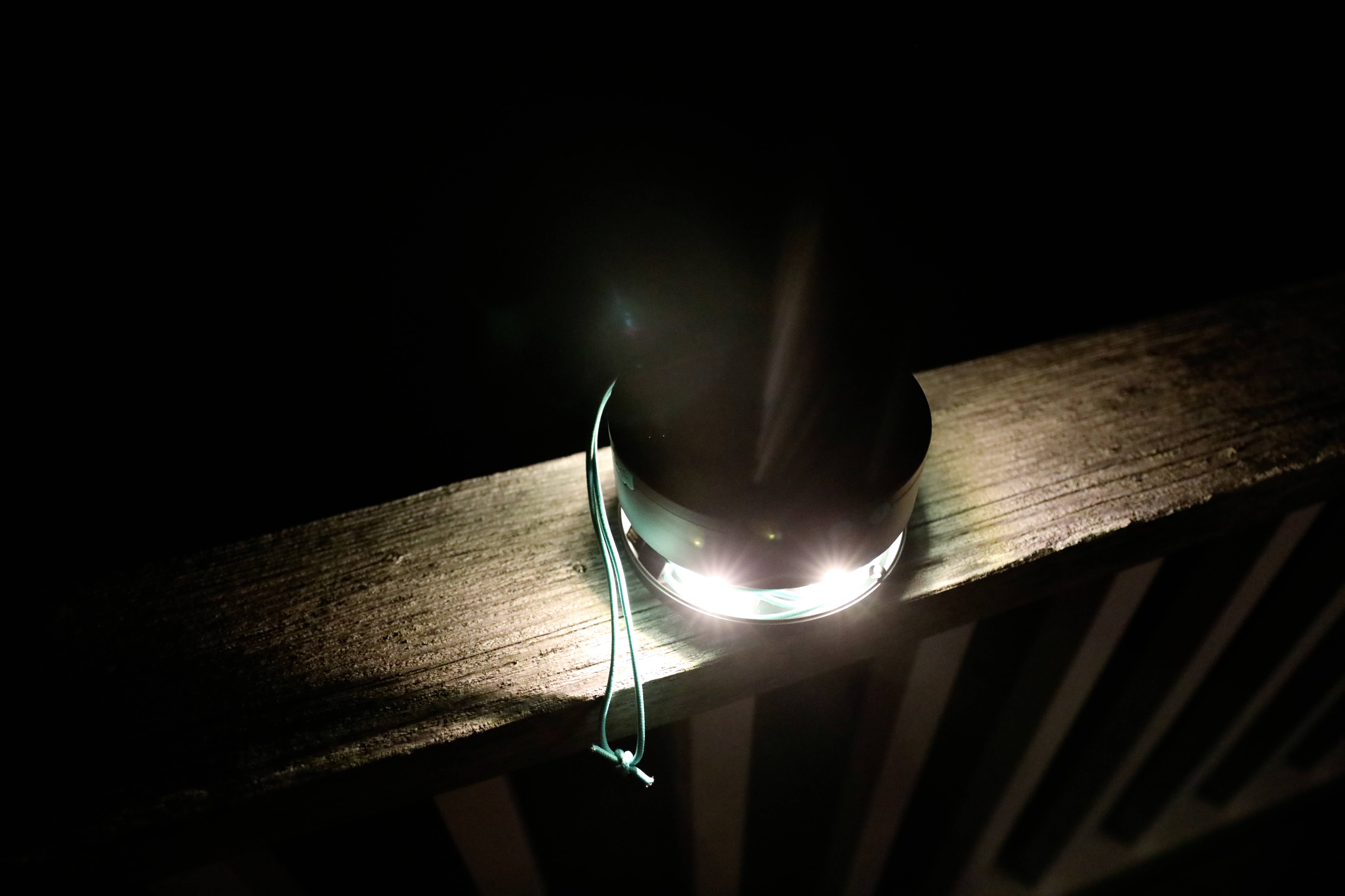 Une petite lampe s'allume sur une rambarde en bois dans l'obscurité. Un ruban bleu est attaché à la lampe.