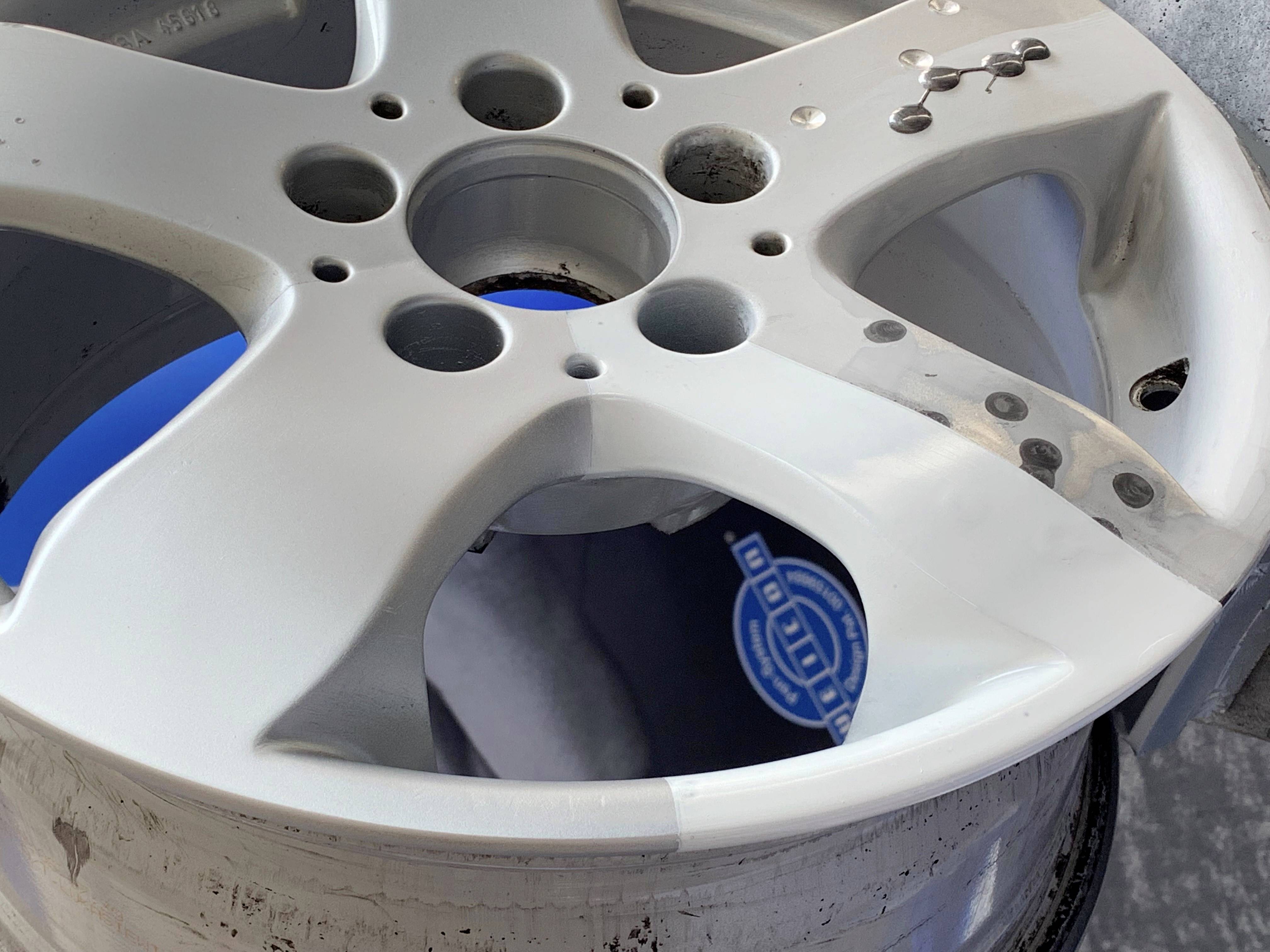Jante d'automobile en argent usée avec plusieurs trous et rayures. Un élément bleu flou est visible en arrière-plan.