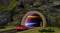 Une voiture rouge roule dans un tunnel éclairé au milieu d'un paysage vallonné. Des panneaux de signalisation indiquent une limitation de vitesse à 80 km/h.