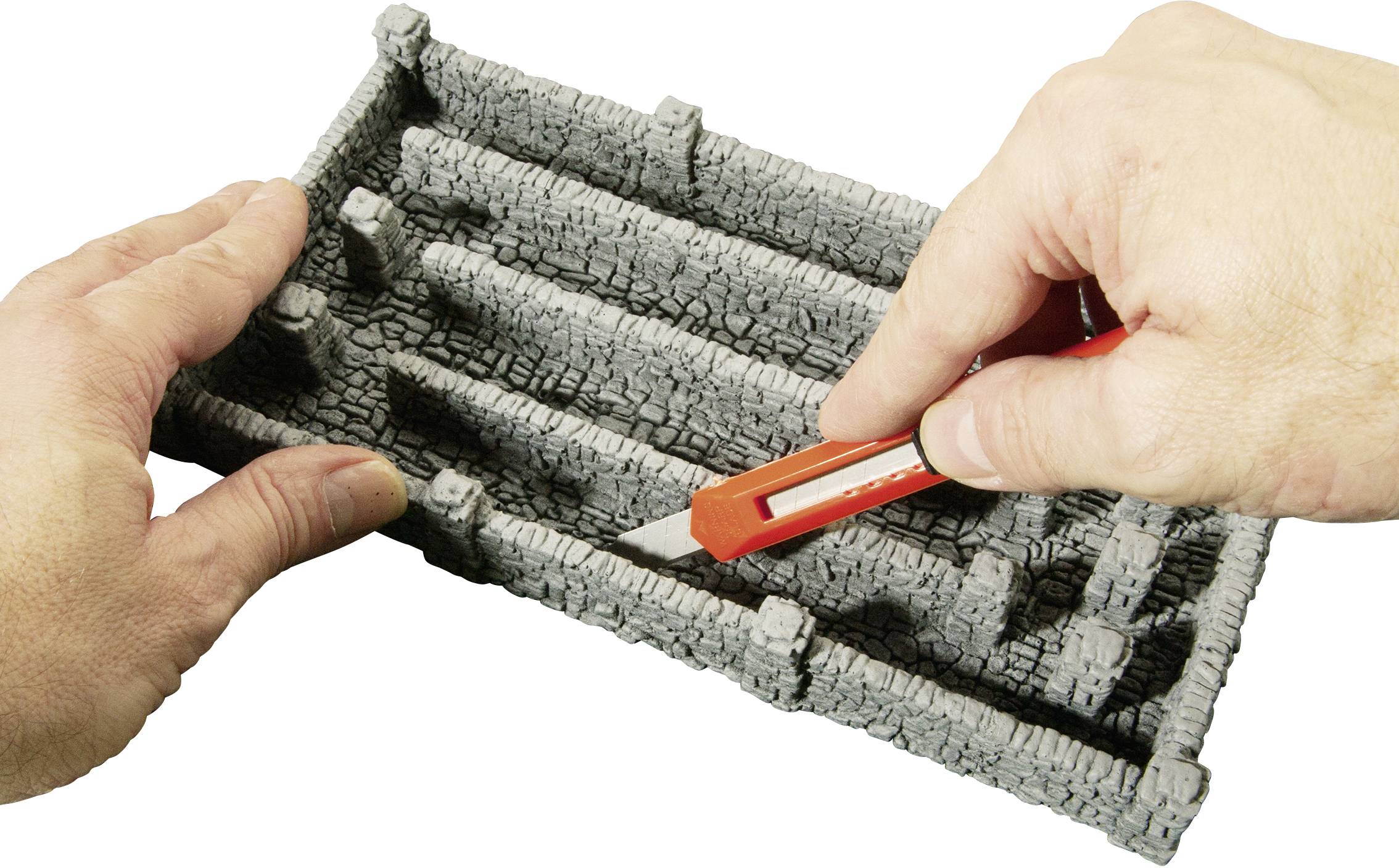 Quelqu'un découpe du polystyrène en forme de labyrinthe à l'aide d'un cutter rouge. Des mains tiennent la pièce pour la travailler.