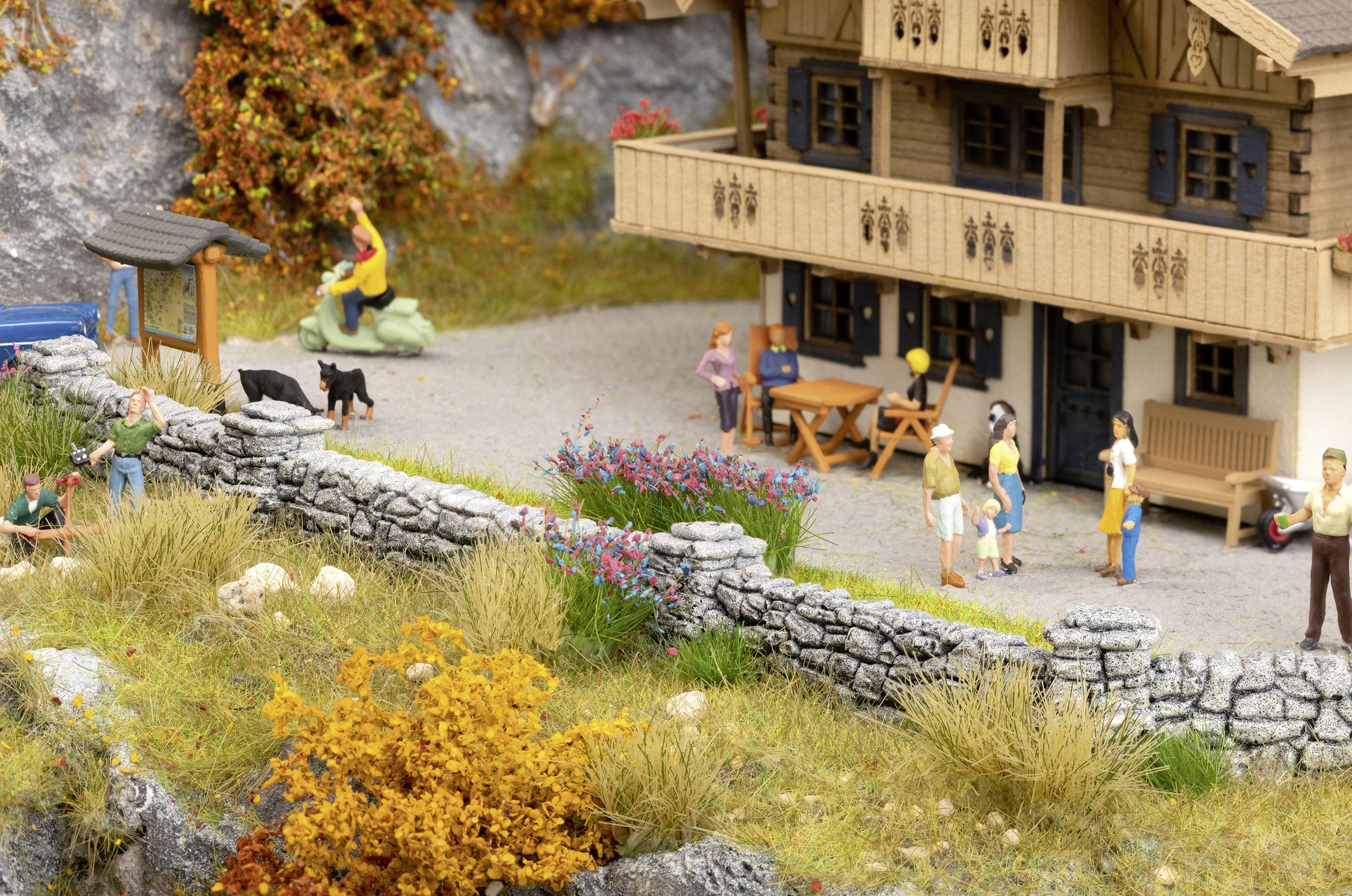 Un modèle d'une maison rurale avec des personnes debout à l'extérieur. Deux chiens noirs sont dans la cour, entourés d'un paysage d'automne.
