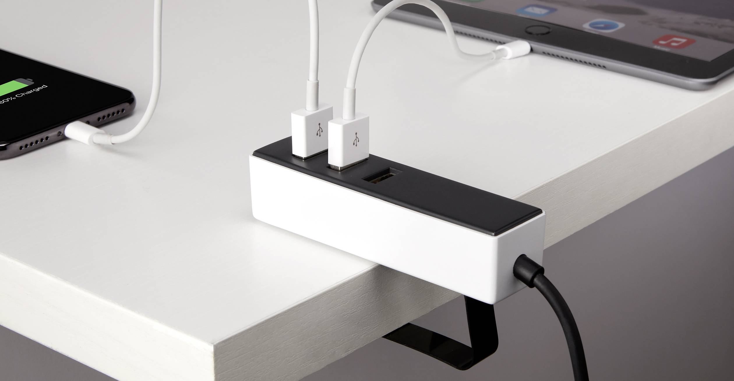 Un organisateur de câbles est fixé à une table, relié à plusieurs câbles qui chargent différents appareils comme une tablette.