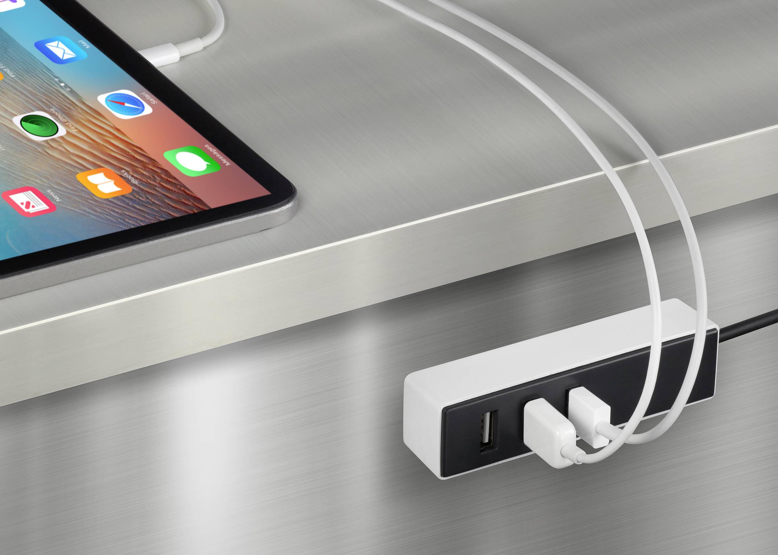 La tablette et le câble de chargement sont branchés à une prise murale. Le câble est connecté à un adaptateur secteur qui repose sur la table.