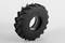 Un pneu de tracteur noir et robuste est dressé verticalement sur un fond gris. Le pneu présente un profil prononcé.