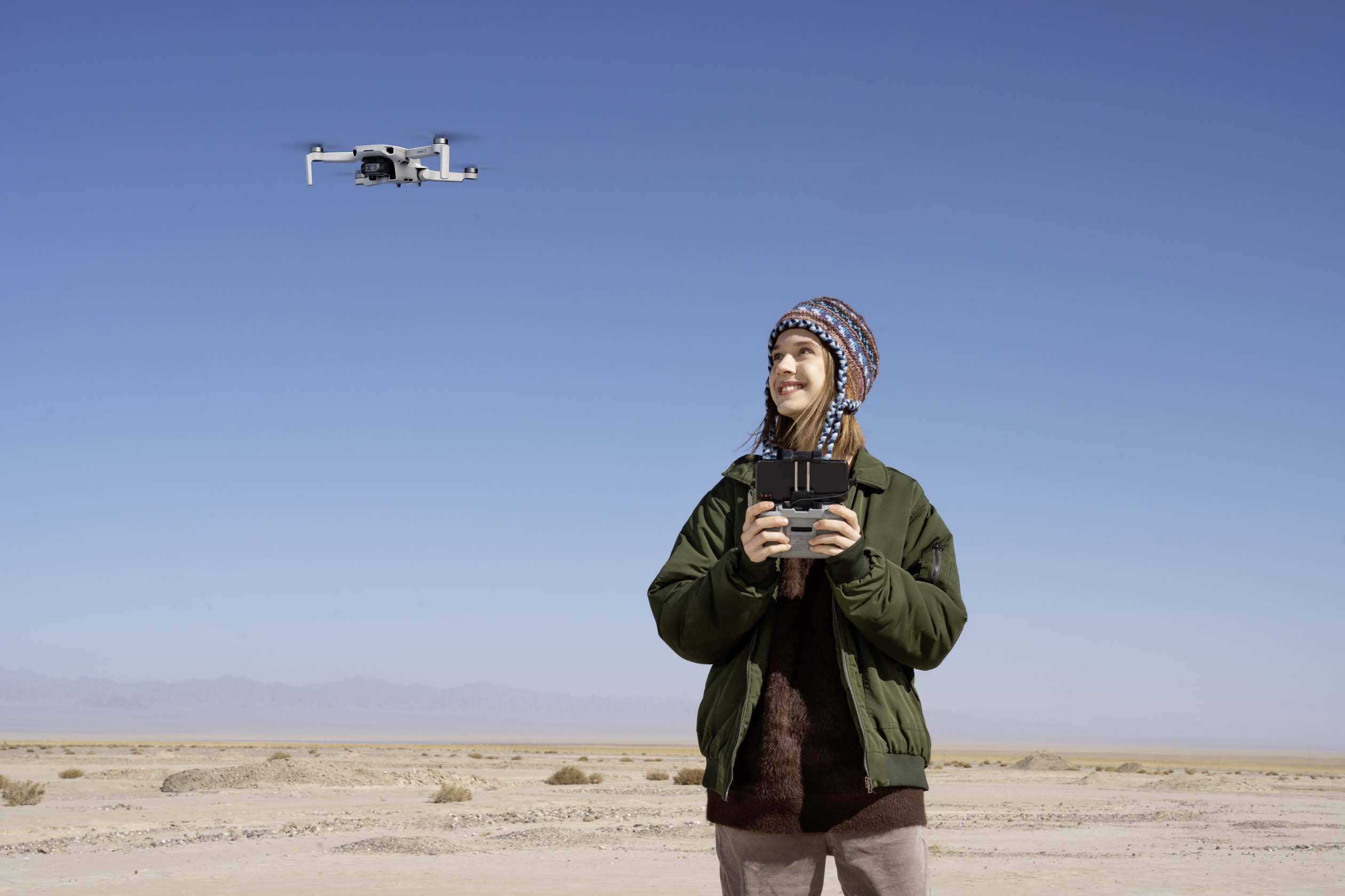 Une personne se tient dans un désert et pilote un drone à l'aide d'une télécommande tout en regardant le ciel.