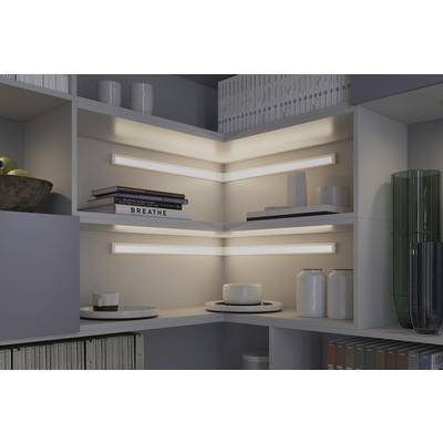 Étagère d'angle avec des tablettes éclairées, sur lesquelles sont disposés des livres, un bol de fruits et des objets de décoration. Design d'intérieur moderne.