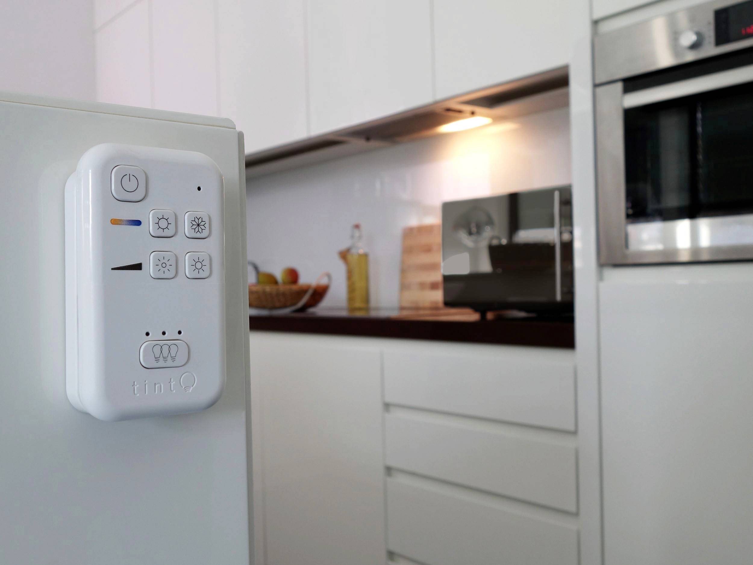 Télécommande blanche sur un réfrigérateur dans une cuisine moderne ; des armoires de cuisine et un four sont visibles en arrière-plan.