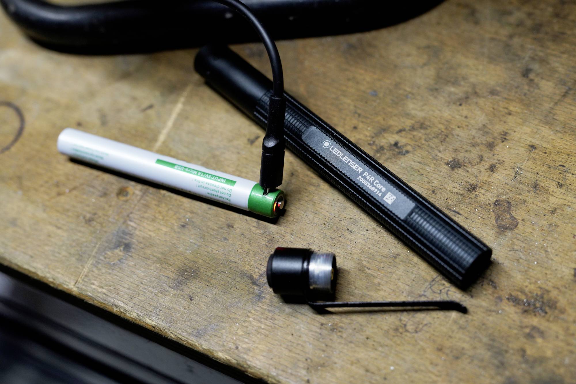 Un chargeur avec une batterie insérée, un câble USB et un couvercle de batterie retiré posés sur une table en bois.