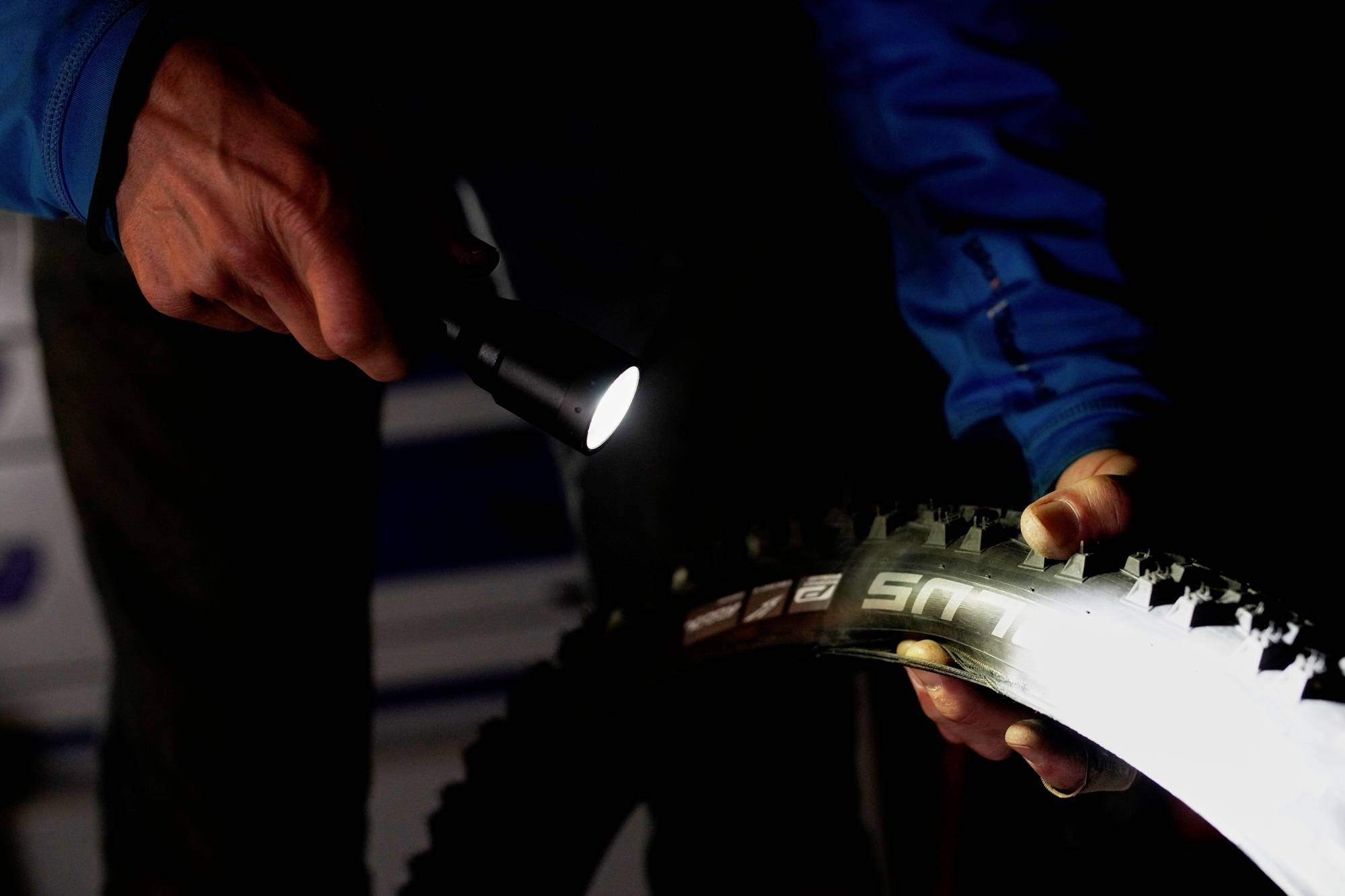 Une personne éclaire un profil de pneu de vélo à l'aide d'une lampe de poche. La marque et le profil du pneu sont visibles, inspectés dans l'obscurité.