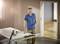 Un homme souriant portant un polo bleu travaille dans une pièce avec une scie circulaire posée sur une table à côté de lui. Il se trouve dans une pièce bien éclairée avec un sol en bois.