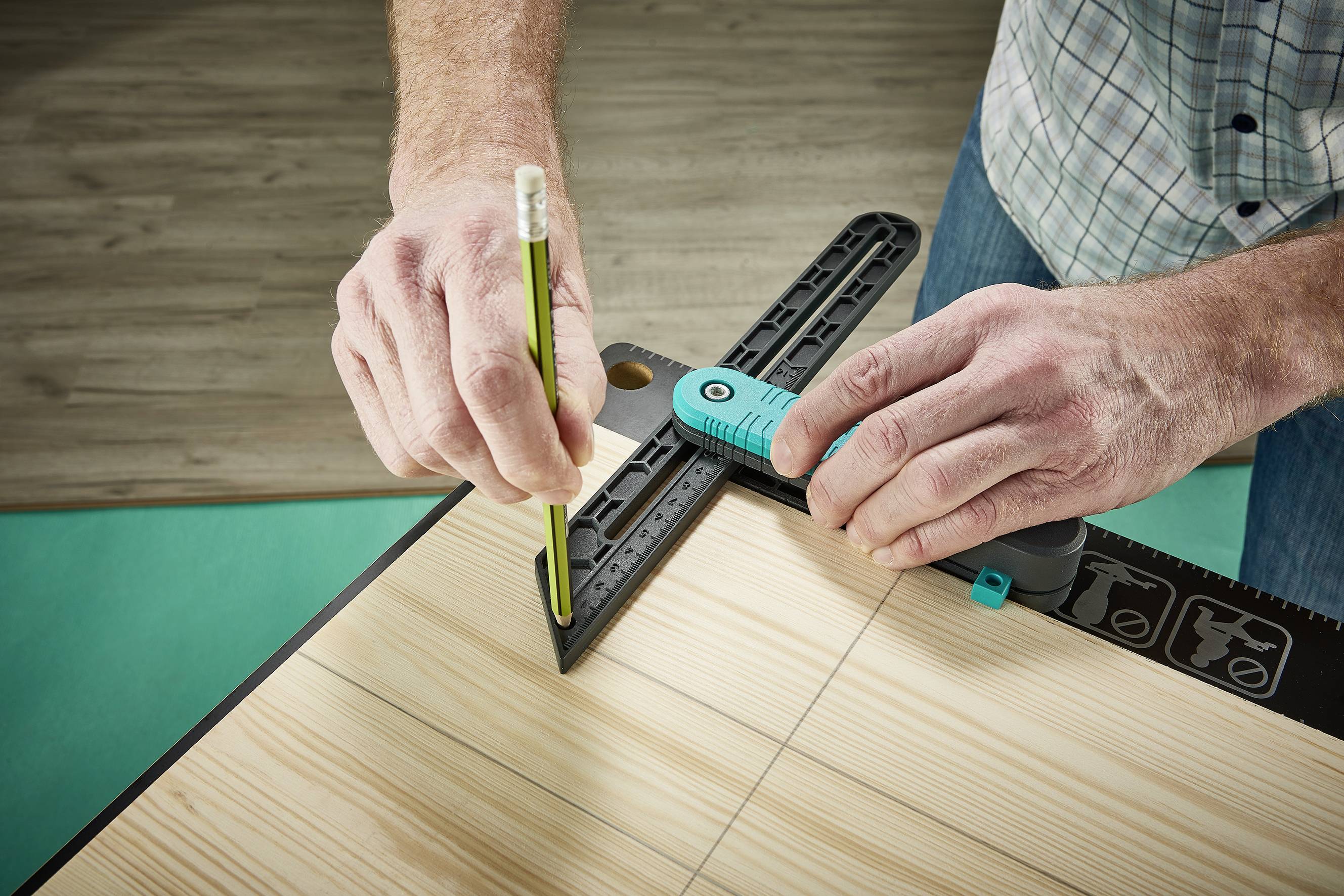 Une personne mesure une planche en bois avec un rapporteur et un stylo vert pour des lignes précises.