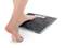 Une personne pose un pied nu sur une balance numérique avec un aspect ardoise sur un fond blanc.
