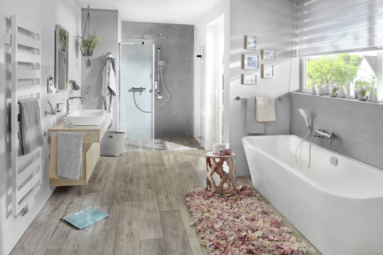 Salle de bain lumineuse avec baignoire, lavabo et douche. Le sol en bois et les décorations apportent une ambiance chaleureuse à la pièce.