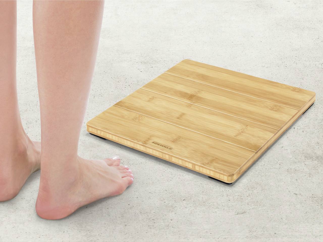Une personne se tient pieds nus à côté d'une balance élégante en bois de bambou sur un sol en béton.