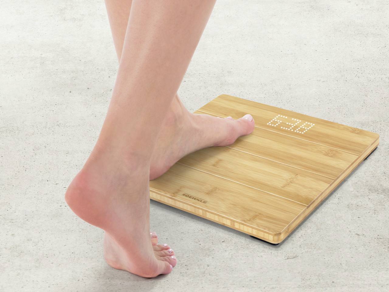 Une personne se tient debout avec un pied sur une balance numérique en bois. La balance affiche un poids.