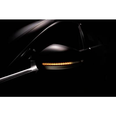 Gros plan sur un clignotant latéral d'une voiture allumé en orange sur un fond sombre.